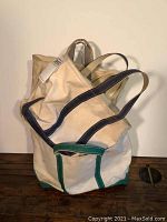 Close-up of two canvas tool bags piled showing natural canvas with green trim and navy blue handles and piping, worn and used