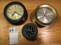 Top view of the three pieces: black Boston marine chronometer, brass Chelsea marine chronometer, black Airguide Chicago compass on wood surface.