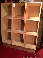Front view of three shelving units each with three open cube compartments on a wooden base.