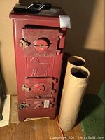 Full view of red Jotul 507B cast iron coal stove with two front doors featuring air vents and embossed horse design. Two pieces of rolled stove pipe beside stove.