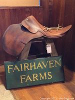 English leather saddle displayed on wooden stepstool with green farm sign in front