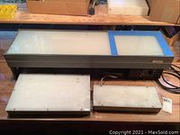 Three light tables shown on a wooden table, featuring one large Richards Model GFL-940 MC Light Table with a metallic frame and two smaller white translucent Porta-Trace light tables.