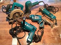 Five Makita power tools displayed on wooden surface, showing overall lot condition and tool variety.