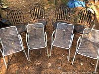 Overview of all 8 chairs outdoors, showing 4 black wrought iron chairs in the back and 4 white vinyl steel chairs in the front.