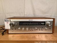 Front view of Sony STR-6055 receiver showing woodgrain cabinet, silver face with tuning display and control knobs.