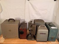 Batch of six vintage movie projectors and data analyzer arranged side by side showing overall size and condition.