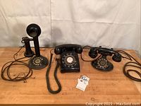Three black rotary telephones on wood table against white backdrop