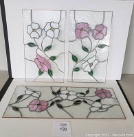 Photo of three floral stained glass panels, one large horizontal and two smaller vertical, showing pink and white flowers with green leaves.