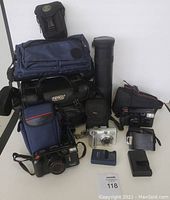 Overview photo showing four cameras with various camera bags and battery chargers all together in one image.