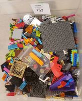 Top view of mixed LEGO pieces in a plastic bin showing various bricks, plates, and small elements in multiple colors and shapes.
