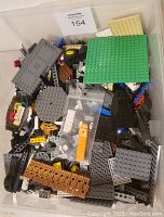 Top-down view of mixed assorted LEGO pieces including base plates, bricks, and the orange separator tool in plastic bag