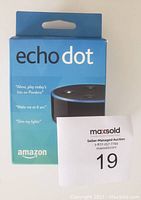 Front view of Amazon Echo Dot 2nd Gen in original blue retail packaging showing product name, Alexa voice commands, and Amazon branding.
