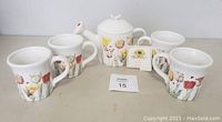 Five items displayed: one Hallmark Nature's Sketchbook teapot surrounded by four matching mugs, all white ceramic with tulip floral designs, shown on a neutral background.
