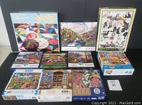 Lot of 10 jigsaw puzzles including one sealed 2000 piece and nine boxed 1000 piece puzzles shown on a table, various colorful scenes on boxes.