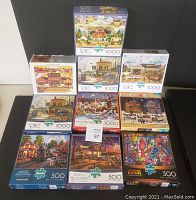 Photo showing 10 boxed jigsaw puzzles stacked, 7 puzzles labeled 1000 pieces and 3 puzzles labeled 500 pieces, all by Buffalo brand with Charles Wysocki artwork.
