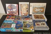 Lot of 11 jigsaw puzzles displayed together showing various themes and piece counts
