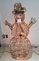 Front view of the light-up outdoor snowman showing the illuminated wireframe, top hat with fabric band, scarf, sunglasses, and button details on the body.
