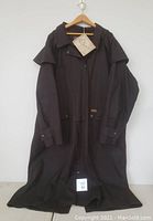 Front view of the men's oilskin duster coat hung on hanger showing button snaps, pockets, and attached tag.
