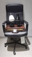 Black Ikea office chair with a brown leather briefcase and two desk lamps (one black, one black with white shade) on the chair seat.