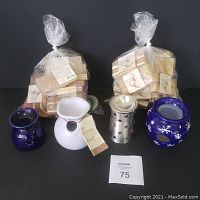 Four wax warmers arranged side by side in front of two sealed bags of wax melts.