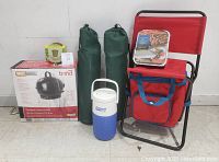 Photo of entire lot showing Bond grill box, two green camp chairs in bags, red folding chair with cooler, Coleman thermos, single-use grill thermos, and citronella candle.