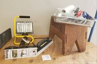 Wide shot showing wooden step stool, yellow-framed portable work light, paint scraper, and metal paint tray with paint rollers and scrapers.