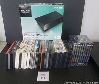 Sony BDP-S1100 Blu-ray/DVD player in original box with assortment of DVDs lined up in front.