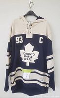 Full front view of the navy and beige Toronto Maple Leafs hooded sweatshirt with lace-up neck, number 93 and captain 'C' on chest, featuring large maple leaf logo in center.