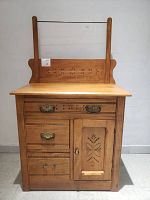 Front view of vintage pine wash stand dresser with carved drawer and cupboard door, visible broken handle on bottom drawer, mirror and towel bar on top.