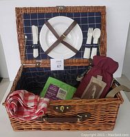 Full view of open wicker picnic basket showing interior contents with 4 wine glasses, tablecloth, napkins, and wine bottle bag