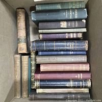 Overhead view of a box filled with assorted antique books showing mostly their spines and cover edges.