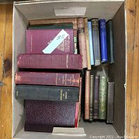 Top-down view into box containing a variety of antique hardcover books with gold embossing and varied colored covers such as red, black, green, and blue.