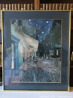 Framed Van Gogh print showing outdoor cafe at night with starry sky, people and cobblestone street.
