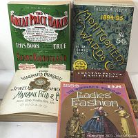 Display of five vintage trade catalogs laid out showing front covers including Sears Roebuck & Co., Montgomery Ward, Marshall Field & Co., Crystal Palace Exhibition, and Ladies Fashion catalogues.