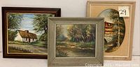 Three framed oil paintings grouped on wall, showing countryside home, pond with forest, and oval mat with covered bridge and cabin