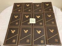 Front view of the 15 brown leather bound books with gold embossed eagle and shield designs arranged in 3 rows of 5 on a white background.
