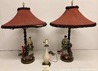 Front view showing pair of Chinese figural lamps with fabric shades and separate embossed floral ceramic lamp with brass base.