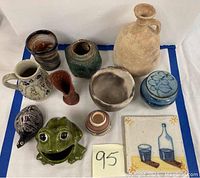 Photo of entire lot of assorted Art Deco pottery and ceramics on white and blue surface including the frog creamer, tile, and various vases