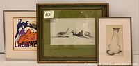 Set of three framed artworks displayed on a surface: abstract print on left, nude drawing center, cat print right.