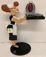 Full view of the lady figurine holding the tray with art glass bottle and candy dish on black base.