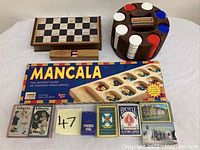 Set showing a wooden chess/checkers board with storage drawer, wooden poker chip holder with chips, a mancala board game in box, and several playing card decks.