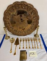 Full lot display with brass plaque, candlesticks, gold wash flatware, and notebook arranged on blue-edged white fabric.