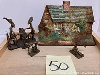 Cast iron door stop and brass figurines together on wooden tray, showing detailed cottage and multiple figurines, with lot number card