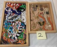 All jewelry items shown arranged in two wooden trays with colorful beaded necklaces and various necklaces, bracelets and brooches visible.