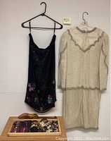 Black sequined dress with floral bead embroidery next to cream embroidered two-piece dress and sewing accessories below