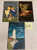 Three hand painted slate art pieces showing a boy and girl with dog, an eagle with banner, and a lighthouse scene