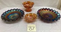Lot of four carnival glass pieces: two ruffled amethyst bowls with iridescent blue and gold tones, one marigold ruffled pedestal vase or compote, and one marigold pedestal candy dish with pressed pattern designs.