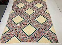 Full view of a patchwork quilt with large diamond shapes outlined in green squares and filled with cream colored triangles.