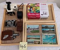 Overview of lot showing three cameras and four stacks of vintage postcards in wooden trays.