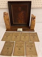 Photo showing artist signed carved wood bookends flanking a framed raised image art piece of a tribesman, with eight Roth Memory Course books spread in front.